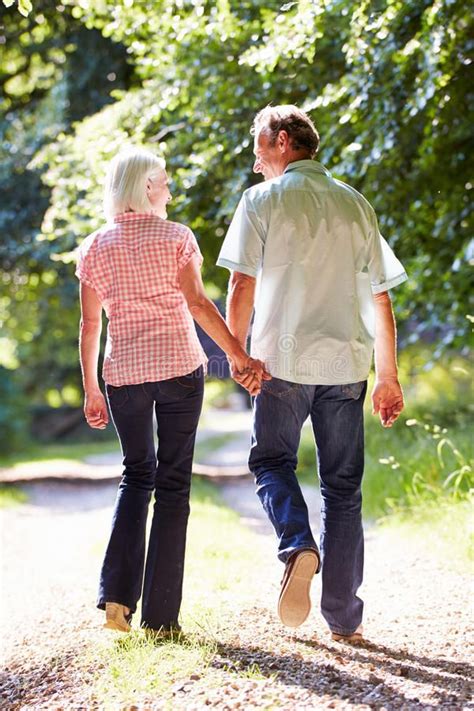 rear view of middle aged couple walking along country lane away from camera hol affiliat