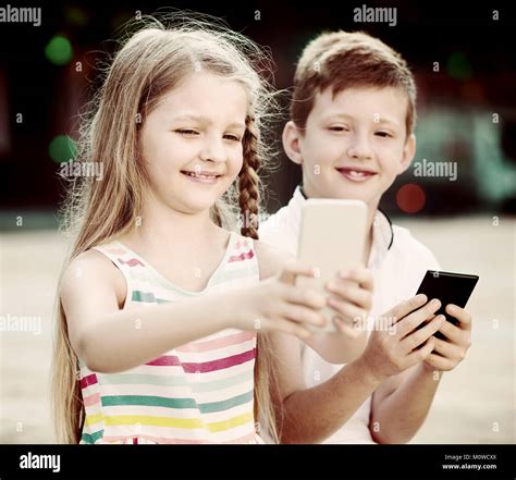 Portrait Of Two Joyful Smiling Kids Busy With Mobile Phones Together