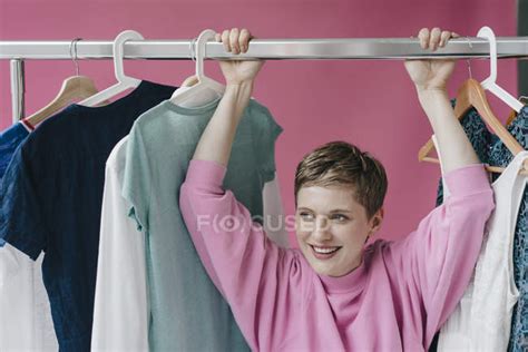 Portrait Of Smiling Woman Hanging On Clothes Rail — Front View