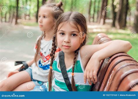 Two Cute Little Girls Sitting On The Wooden Bench In Park Stock Image