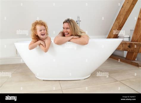 Mother And Daughter Looking Over The Edge Of A Freestanding Bath Tub In