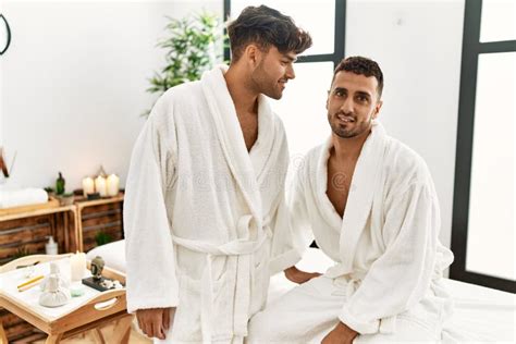 Two Hispanic Men Couple Wearing Bathrobe Sitting On Massage Table At