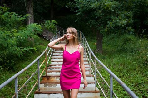 A Slender Girl In A Pink Dress Going Down The Stairs In The Alley Of