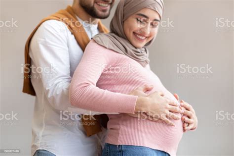 Happy Arab Husband Hugging Pregnant Wifes Belly On Gray Background