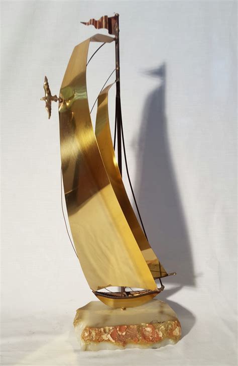 A Golden Sailboat Sculpture On A White Background With A Shadow From