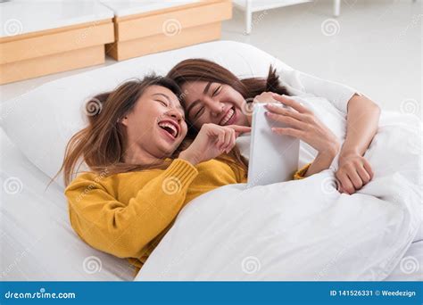 la coppia lesbica asiatica del lgbt che si trova insieme sul letto facendo uso del computer