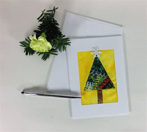 A Card With A Christmas Tree On It Next To A Pen And Some Flowers In