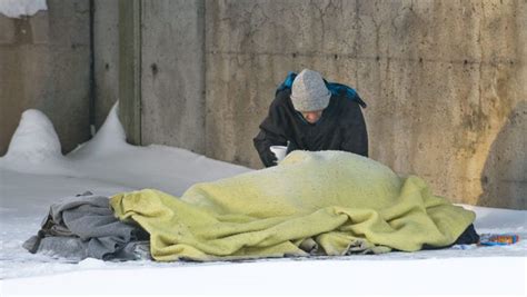 A Man Checks On A Homeless Person Sleeping On A Snow Covered Sidewalk