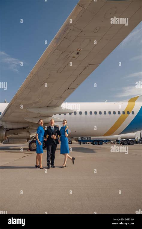 Full Length Shot Of Pilot Standing Together With Two Stewardesses In