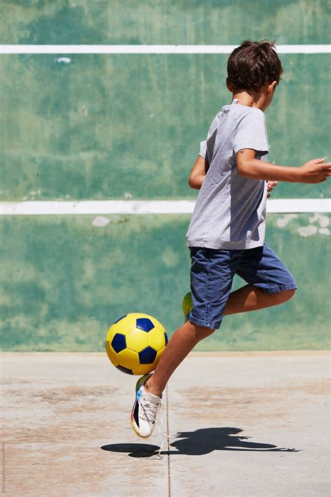 Unrecognizable Boy Playing Football On Asphalt By Stocksy Contributor