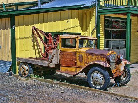 An Old Rusted Truck Parked In Front Of A Yellow Building With A Crane