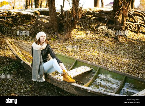slim girl in blue jeans brown jacket and boots sat on the upturned boat on the shore yellow