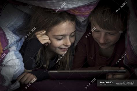 Brother And Sister Lying Side By Side Using Digital Tablet Under A
