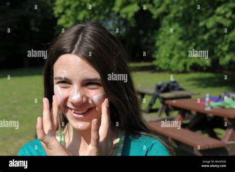 Girl Happily Applying Suncream To Protect Her Face From Sunburn In A Park On A Hot Sunny Day