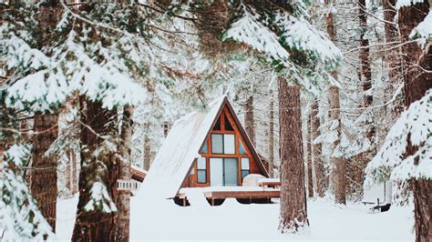 A Small Cabin Nestled In The Woods Covered In Snow