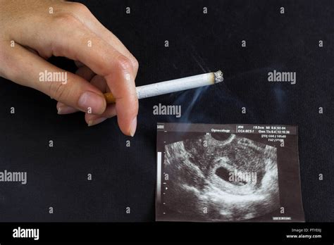 a woman s hand holds a burning cigarette against the background of a picture of the uzi of