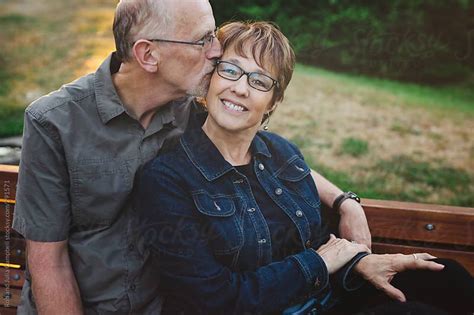 middle aged retired couple kissing and cuddling outside sitting on a bench by rob and julia