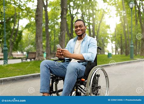 Happy Disabled Black Man In Wheelchair Using Smartphone Checking Messages Online At Park Stock