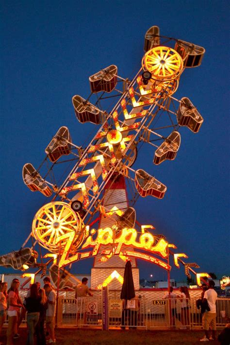 An Amusement Park Ride At Night With People Standing Around It