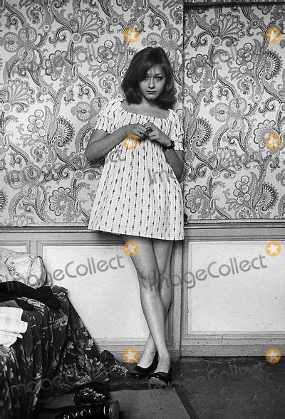A Woman Standing Next To A Bed In A Room With Wallpaper And Shoes On The Floor