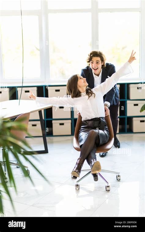 Businesswoman Pushing Playful Colleague In Office Chair Stock Photo Alamy