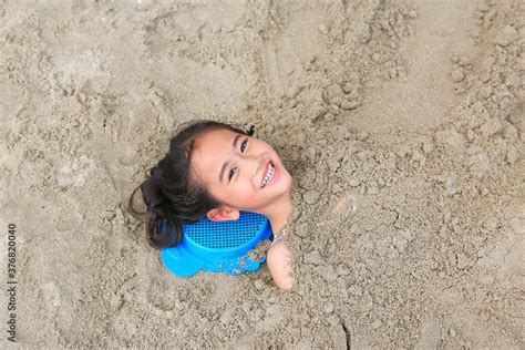 Portrait Of Happy Asian Little Child Girl Buried In The Sand At The