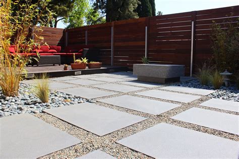 An Outdoor Patio With Stone Pavers Gravel And Wood Privacy Fence In