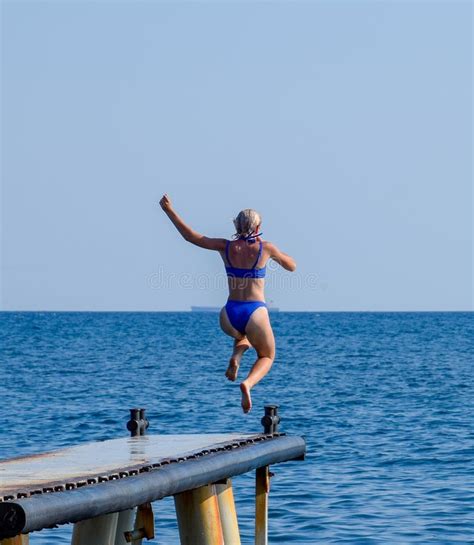 A Beautiful Girl In A Blue Bikini Jumps From The Pier Into The Water Jumping In The Sea Stock