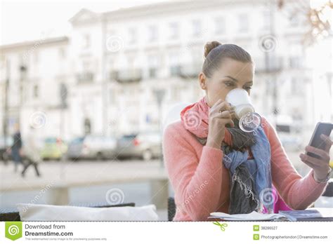 Young Woman Drinking Coffee While Using Cell Phone At Sidewalk Cafe
