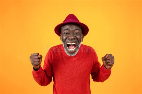 cheerful excited old black man in hat with open mouth scream rise fists celebrate win stock