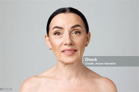 smiling beautiful mature woman with bare shoulders looking at camera over grey background