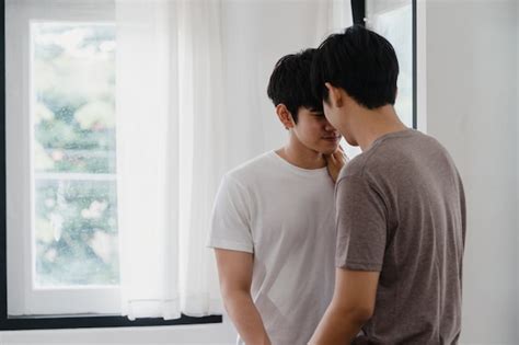 アジアの同性愛者のカップルに立って、自宅の窓の近くを抱いて。若いアジアのlgbtq 男性が幸せにキスをしてリラックスして休憩を一緒に朝のモダンな家のリビングルームでロマンチックな時間を過ごし