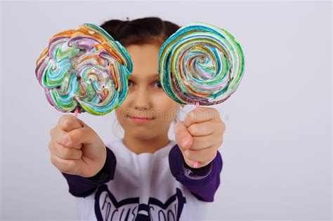 A Girl Holds In Two Hands Multicolored Candies On A Stick Showing Them