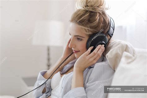 Portrait Of Smiling Blond Woman Sitting On Bed Hearing Music With