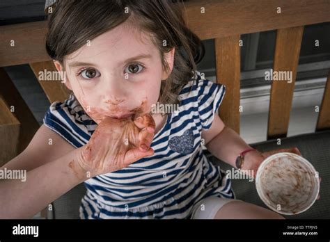 High Angle Portrait Of Girl With Messy Mouth Eating Chocolate While Sitting On Chair At Home