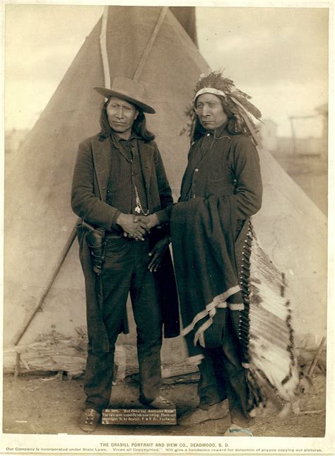 two native americans standing next to each other in front of a teepee