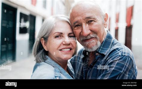 Happy Multiracial Senior Couple Hugging Each Other With City On Background Elderly People