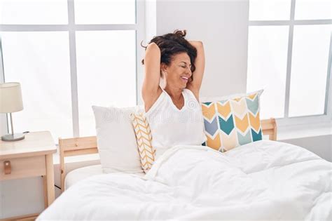 Middle Age Woman Waking Up Stretching Arms At Bedroom Stock Photo