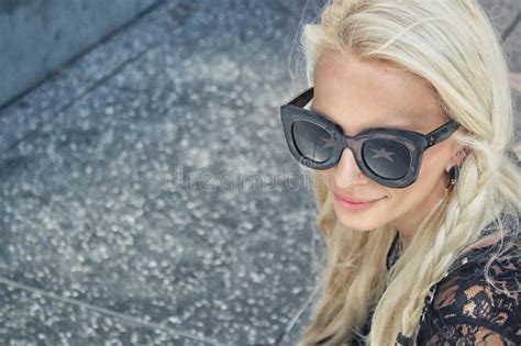 Woman Wearing Black Framed Wayfarer Style Sunglasses And Black Floral Top Near Gray Concrete