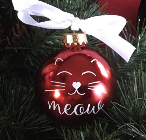 A Red Ornament Hanging From A Christmas Tree With A Cat Face On It