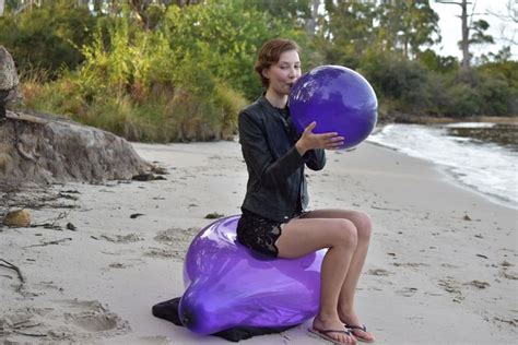 Blowing A Purple Balloon Up While Sitting On Another Purple Balloons