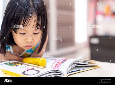 Asian Girl Child Reading Interactive Book In Living Room At Home As