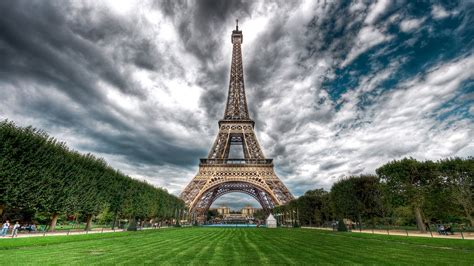 Eiffel Tower With Green Grass Field On Front With Background Of Clouds