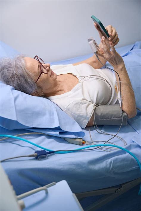 Elderly Woman Is Chatting On Mobile Phone From Hospital Room Stock