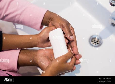 Grandmother And Granddaughter Washing Hands With Soap In Bathroom Sink