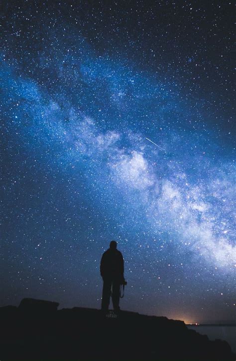 A Man Standing On Top Of A Hill Under A Night Sky Filled With Lots Of Stars