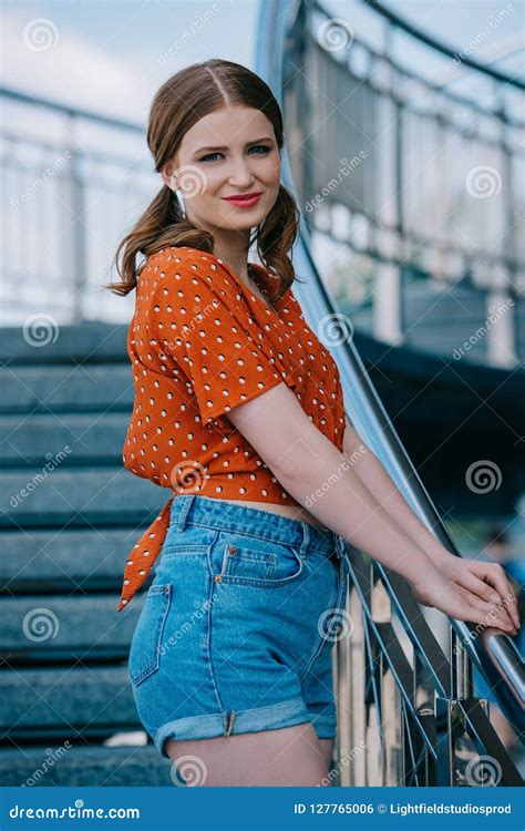 Beautiful Stylish Girl In Denim Shorts Standing On Stairs And Smiling