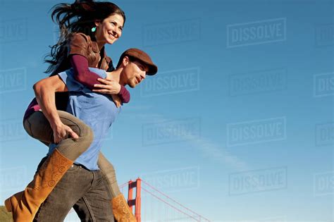 Man Carrying Woman On His Back Near Golden Gate Bridge Stock Photo