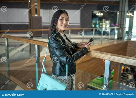 Young Brunette Female Leaning On Stair Rails Checking Her Smartphone