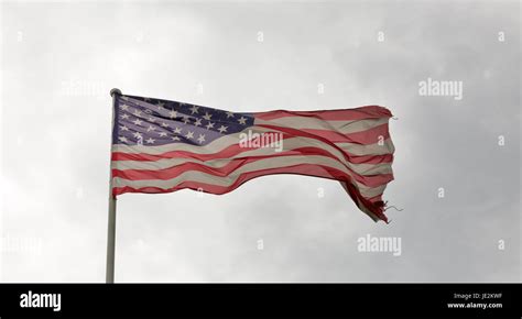Faded And Tattered American Flag Waving Against A Cloudy Sky Stock